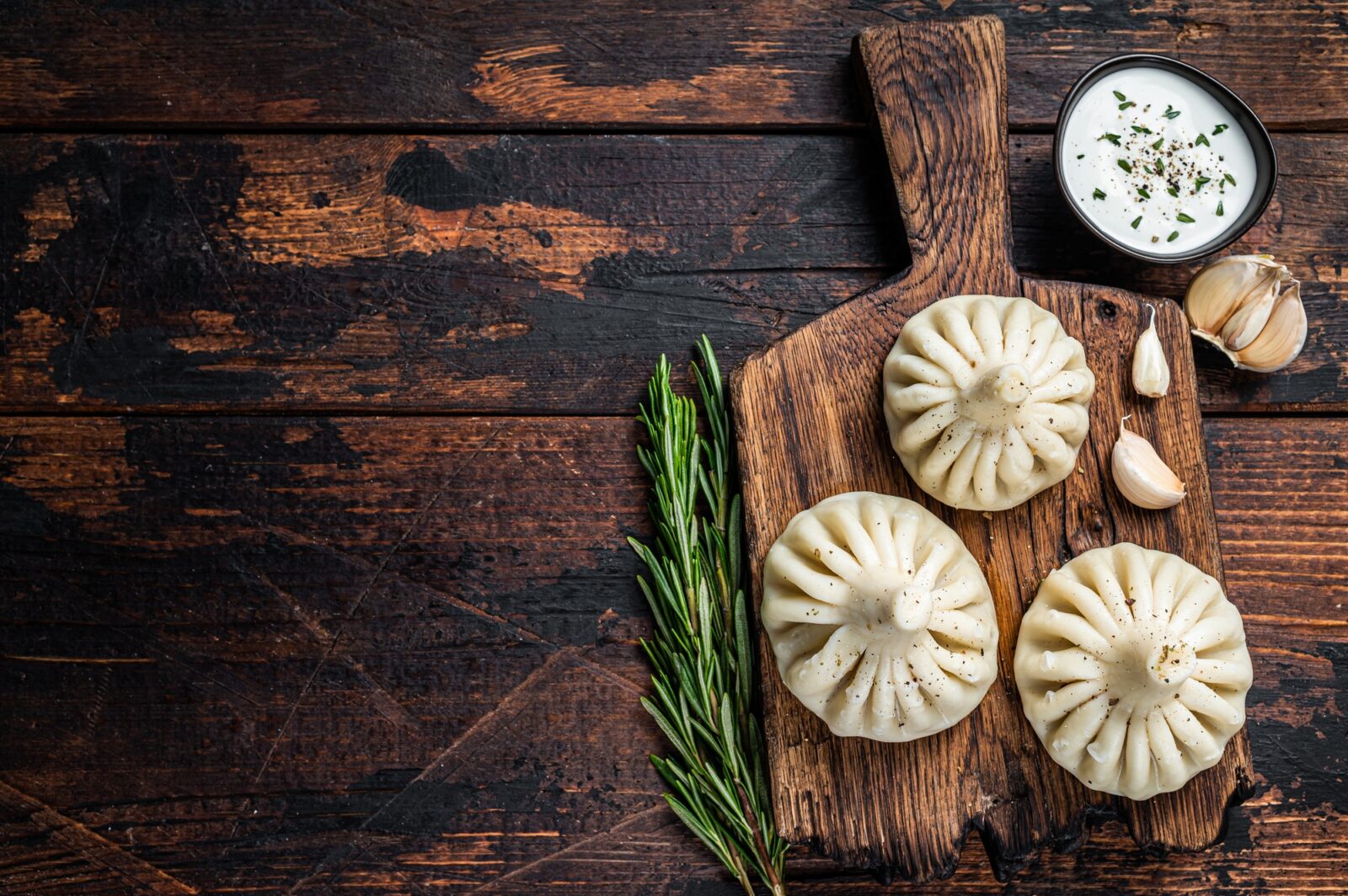 Georgian Khinkali Dumplings with beef and lamb meat on wooden board with herbs.
